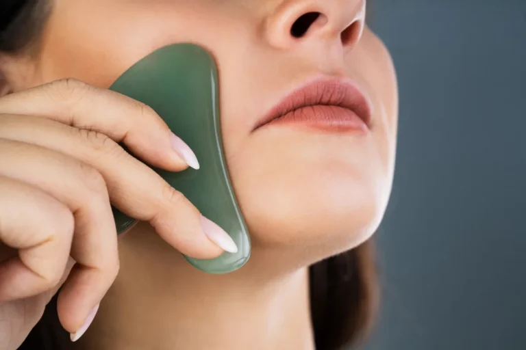 Frau streicht mit einem grünen Gua-Sha-Stein über Wange und Kieferlinie